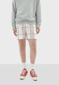 Grijze sweatshirt, geblokte short in wit met rode, groene en blauwe lijnen, witte sneakersokken en rode canvas sneakers met witte zolen.