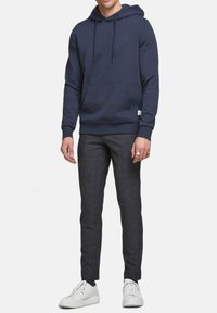 Hoodie marine avec cordons de serrage et poche avant, associé à un pantalon ajusté à motifs et des sneakers blanches. Texture de tissu lisse, design décontracté.