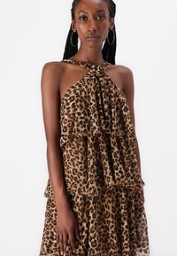 Leopardmönstrad halterneck-klänning med knuten halsringning, lager av volanger, genomskinlig textur och färgpalett i brunt och svart. Kort längd.