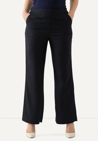 Mörkblå nålstripade byxor med rak ben-design, sidofickor och en slät textur. I kombination med krämfärgade klackar.