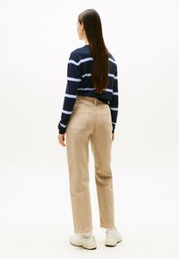 Camisa de rayas marinas de manga larga con rayas azul claro, combinada con pantalones de tiro alto beige y zapatillas blancas, vista desde atrás.