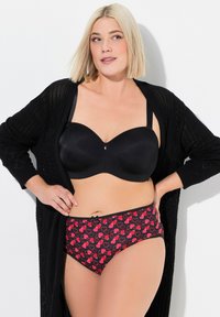 Reggiseno imbottito nero in tessuto liscio con spalline regolabili, abbinato a mutandine a vita alta con un motivo a cuori rossi su sfondo nero.