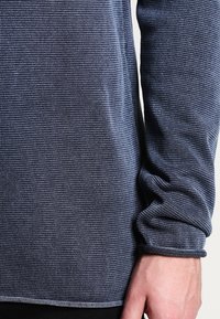 Mörkblå långärmad skjorta med en strukturerad, stickad modell. Har formsydda manschetter och nederkant, med synliga sömmar.