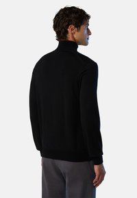 Maglione nero a maglia con colletto alto e maniche lunghe. Il materiale sembra morbido con una consistenza liscia. Design semplice, senza motivi o decorazioni visibili.