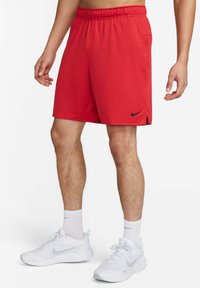 Uomo che indossa pantaloni corti sportivi rossi Nike, calze bianche Nike e scarpe da corsa bianche Nike, in piedi con le mani rilassate ai lati.
