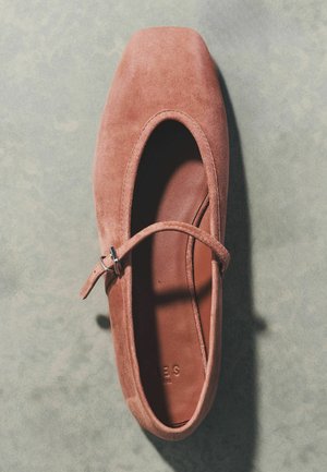Scarpa singola Mary Jane piatta in camoscio rosa polveroso con cinturino e fibbia, vista dall'alto su una superficie grigia testurizzata.