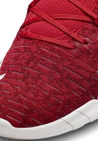 Gros plan d'une basket rouge tricotée avec un motif texturé et des lacets rouges sur une semelle blanche segmentée.
