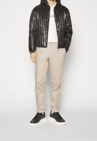 Svart pufferjacka med huva och quiltat mönster, ihop med beiga byxor och svarta sneakers med vita sulor.