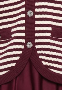 Μπορντό και λευκή ραβδωτή πλεκτή ζακέτα με υφασμάτινα ασημένια κουμπιά σε σχέδιο λουλουδιού και ταιριαστό μπορντό ύφασμα από κάτω.