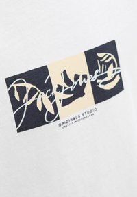 Biela bavlnená tričko s grafickým dizajnom v námorníckej modrej a béžovej farbe, s typografickým logom a abstraktnými tvarmi.