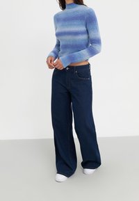 Blårandig stickad tröja med hög hals och långa ärmar, kombinerad med vida mörk denimjeans och vita sneakers.