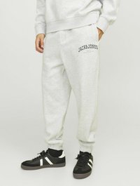 Pantaloni della tuta grigi con vita e polsini elasticizzati, caratterizzati da un logo nero "JACK & JONES" sulla coscia. Indossati con scarpe da ginnastica nere.