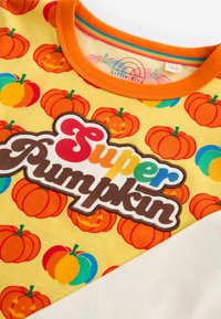 Gelbes T-Shirt mit einem Allover-Kürbisdruck, einem leuchtend orangefarbenen Halsausschnitt und einem mehrfarbigen "Super Pumpkin"-Logo in unterschiedlichen Texturen.