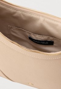 Interno di borsa beige testurizzata con chiusura a zip dorata, con etichetta nera recante la scritta "ANNA FIELD" e una fodera morbida.