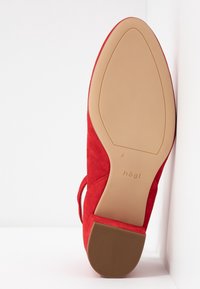 Semelle de chaussure femme en daim rouge avec un petit talon bloc, semelle beige lisse et nom de marque « hōgl » visible près de la voûte plantaire.