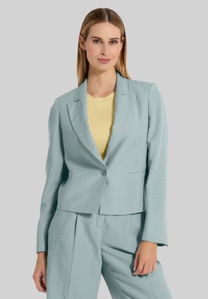 Lichtblauwe blazer van gestructureerde stof, met één knoopsluiting en twee voorzakken, gecombineerd met een gele top, tegen een neutrale achtergrond.