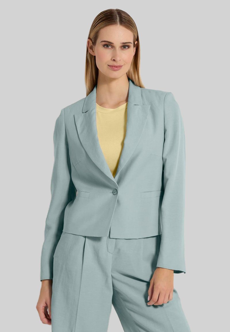 Lichtblauwe blazer van gestructureerde stof, met één knoopsluiting en twee voorzakken, gecombineerd met een gele top, tegen een neutrale achtergrond.