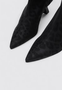 Botas negras hasta el tobillo con punta afilada, hechas de un material texturizado con un sutil patrón de leopardo y un tacón bajo tipo bloque.