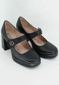 Décolleté Mary Jane in pelle nera con punta quadrata, tacco a blocco spesso e cinturino regolabile con dettagli circolari in metallo.