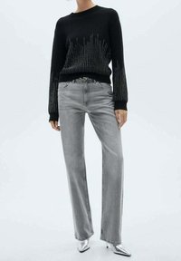 Schwarzer Strickpullover mit metallischen Akzenten am Saum, kombiniert mit hellgrauen, geraden Jeans und silbernen, spitzen Heels.