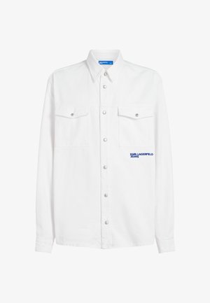 Fehér, gombos pamuting, két mellzsebbel, ezüst patentgombokkal és a bal oldalon kék logós felirattal.