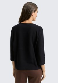 Schwarzer, strukturierten Pullover mit Dreiviertelärmeln und weiter Ausschnitt, von hinten betrachtet. Keine sichtbaren Muster oder Hardware-Details.