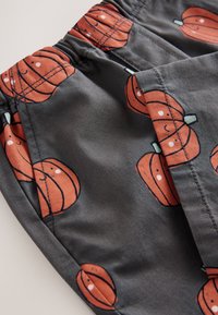 Shorts en tissu gris ornés d'un imprimé citrouille orange souriant sur l'ensemble. Ceinture élastique avec détails de couture et poche latérale.