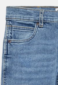 Pantalones de mezclilla azul claro con un diseño clásico de cinco bolsillos, que presentan costuras de cobre y un cierre de botón en la cintura.