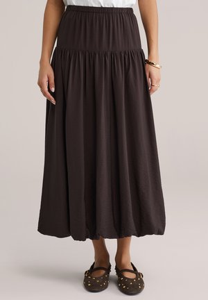 Czarna spódnica do kostek z elastycznym pasem i marszczonym wzorem, wykonana z lekkiego materiału; zestawiona z płaskimi butami niskimi na okrągły nosek, ozdobionymi ćwiekami.