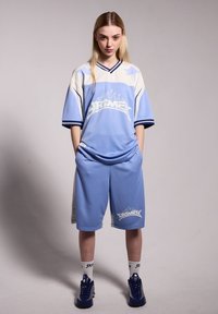 Conjunto deportivo azul claro que incluye una camiseta de mangas cortas con acentos y logotipo en blanco, combinada con pantalones cortos sueltos, ambos en un tejido suave.
