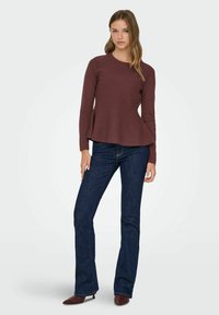 Bordeauxrotes Langarmtop mit ausgestelltem Saum, kombiniert mit dunkelblauen ausgestellten Jeans. Das Outfit zeichnet sich durch eine glatte Textur und eine figurbetonte Silhouette aus.