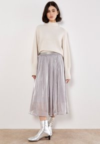 Jersey de punto texturizado de color beige claro, combinado con una falda midi de plata con pliegues y botines de cuero plateados brillantes. El material presenta un acabado metálico suave.