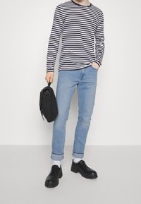 Långärmad tröja i marinblå och vit rand, ljusblå jeans, svarta skor, håller en svart väska, med uppvikta ärmar och vita strumpor.