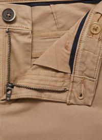 Tissu beige avec une poche zippée et une fermeture à bouton. Présente une taille contrastante foncée, des coutures décoratives et de multiples détails de poches.