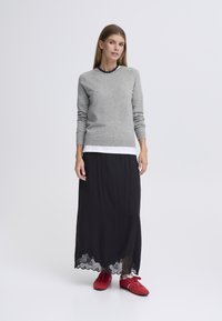 Pull en maille gris, jupe longue noire avec ourlet en dentelle, et baskets rouges. La tenue associe des textures douces et des couleurs contrastées.