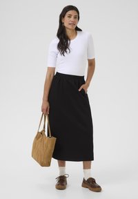 Jupe midi noire à taille élastique, haut ajusté blanc à manches courtes, chaussures en cuir marron à lacets, sac fourre-tout beige, chaussettes blanches arrivant au genou, textures lisses.