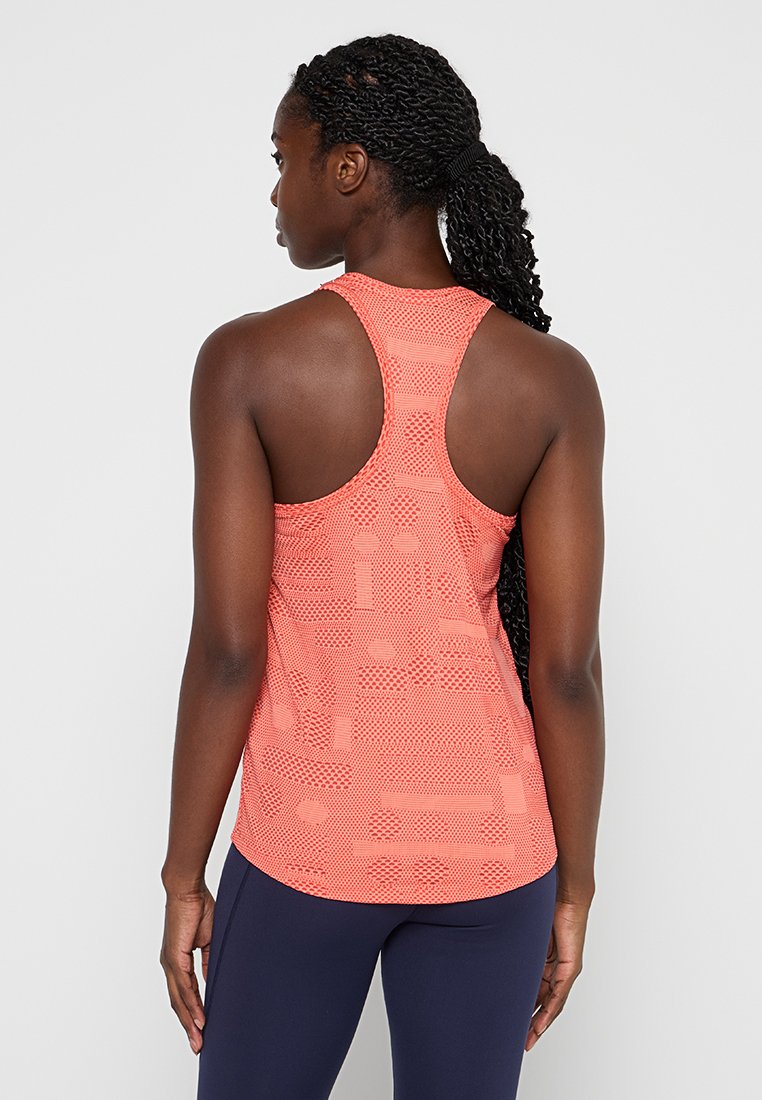 Racerback-Top in leuchtendem Koralle mit strukturiertem Muster, aus atmungsaktivem Material und figurbetonendem Schnitt, kombiniert mit marineblauen Leggings.