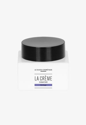 Weißes quadratisches Kosmetiktiegel mit schwarzem Deckel. Vorderseite mit dem Text: "LA CRÈME SIGNATURE" und unten in Lila "Héritage".
