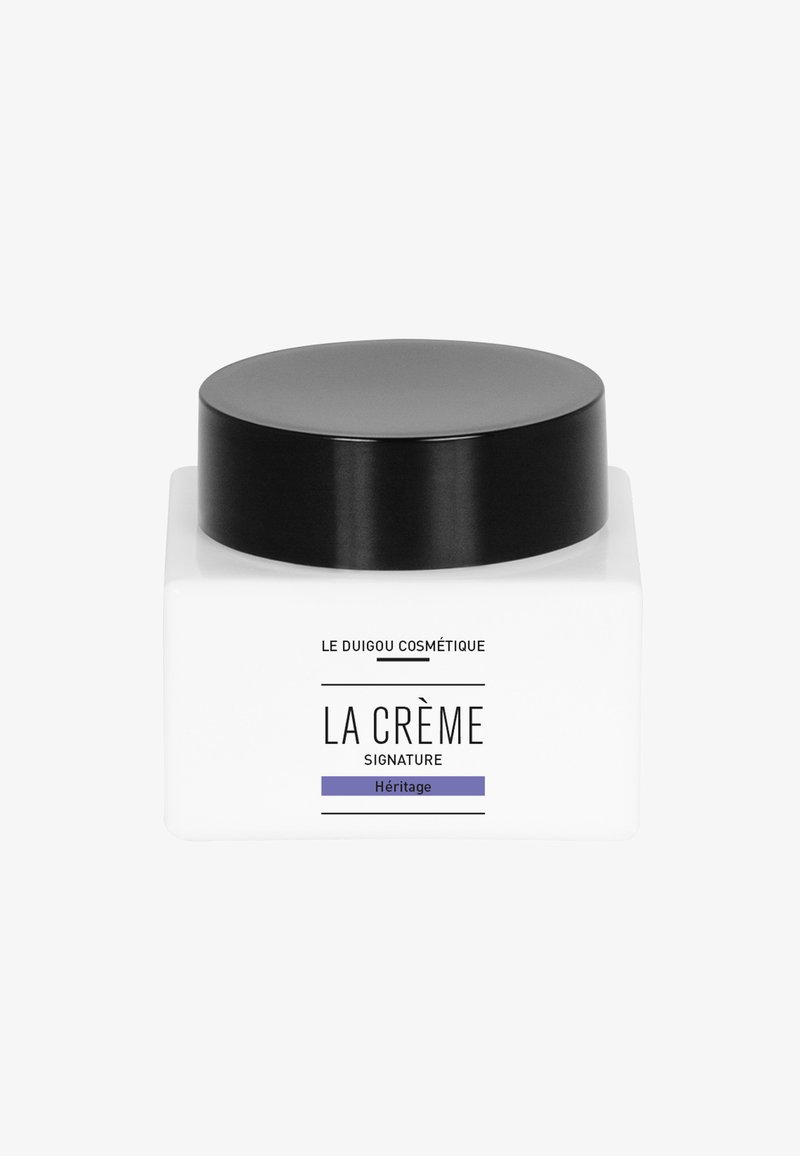 Weißes quadratisches Kosmetiktiegel mit schwarzem Deckel. Vorderseite mit dem Text: "LA CRÈME SIGNATURE" und unten in Lila "Héritage".