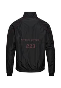 Zwarte jas met hoge kraag, voorzien van kastanjebruine stiksels. Tekst op de achterkant omvat "OFF DUTY OFF PITCH" en "223." Elastische zoom en manchetten.