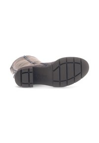 Donker rubberen zool met een textuurpatroon voor grip. Bovenste gedeelte is gemaakt van een zacht, lichtgekleurde materiaal met een ritsdetail aan één kant.