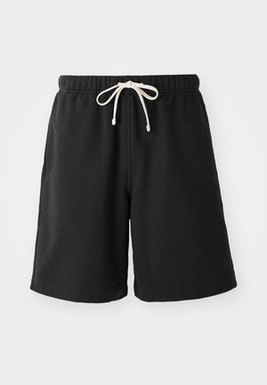 Fekete melegítőnadrág puha anyagból, rugalmas derékpánttal, krémszínű zsinórral és oldalsó zsebekkel.