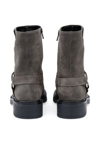Bottines en daim gris avec une finition mate, dotées de semelles en caoutchouc noir, de zips latéraux et de sangles décoratives avec des accents métalliques.