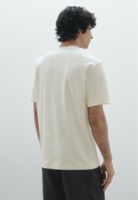 T-shirt a maniche corte di colore crema, realizzato in un tessuto morbido. Presenta un collo rotondo, una vestibilità comoda e spacchi laterali per maggiore comfort.