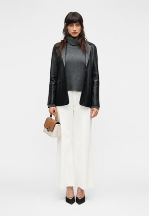 Μαύρο δερμάτινο σακάκι, γκρι πλεκτό μπλουζάκι με λαιμόκοψη, λευκό παντελόνι με φαρδιά πόδια, μαύρα τακούνια και τσάντα με μοτίβο και καφέ λεπτομέρειες.