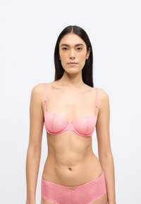 Rózsaszín csipkés melltartó geometriai mintával, alátámasztó merevítőkkel, hullámos széllel és állítható pántokkal, hozzáillő csipkés rövidnadrággal párosítva.