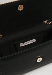 Interior de bolso de cuero negro con textura suave, con cierre a presión en tono dorado y una etiqueta de marca en un bolsillo lateral.