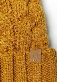Musztardowo-żółta dziana czapka z warkoczem, wykonana z teksturowanej, grubej włóczki, z małą skórzaną metką z wytłoczonym literą "M."