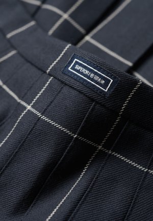 Navy blue plaid trousers with white lines, featuring a sewn label that reads "SUPERDRY." Fabric texture is smooth and sturdy.