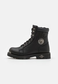 Bottines à lacets en cuir noir avec un design de flammes surélevées, quincaillerie en acier inoxydable et un accent décoratif en métal en forme de crâne sur le talon.